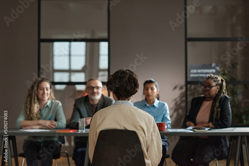 Rear view of young man sitting on chair opposite business people who asking him questions during job interview