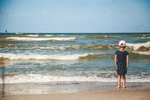 Little girl standing alone on the beach of a Baltic sea