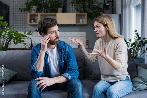 Family quarrel, woman quarrels and yells at the loser's husband, couple at home sitting in the living room on the couch