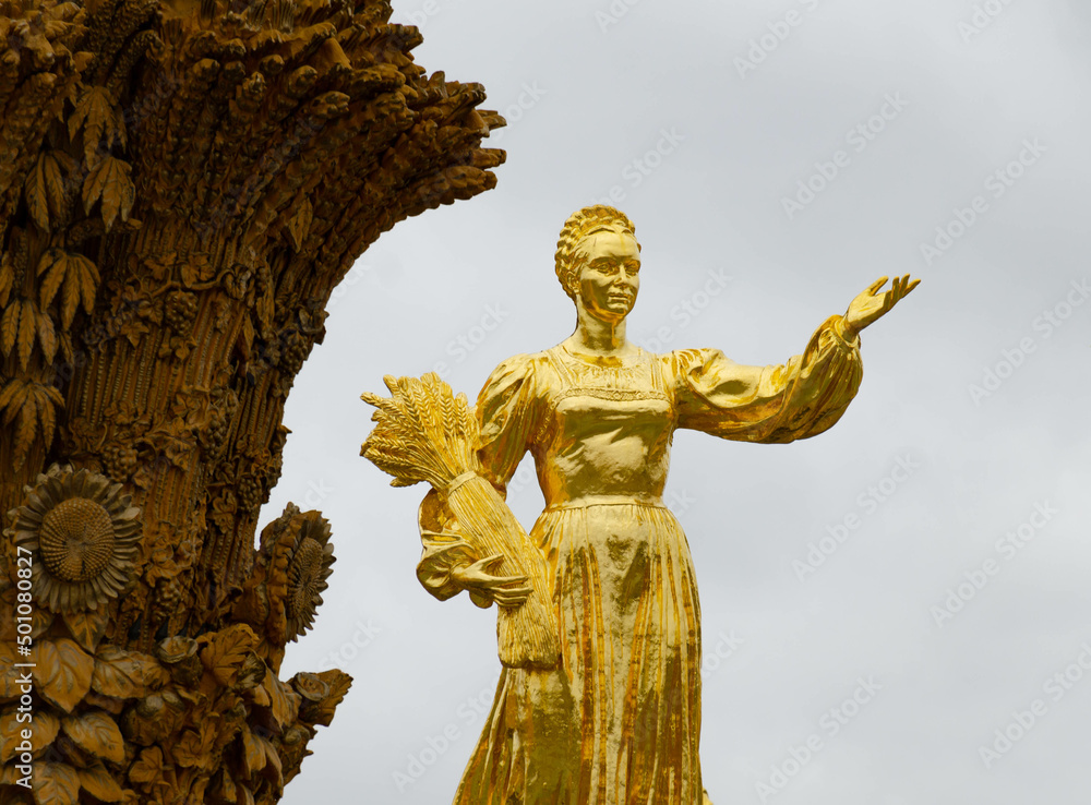 Obraz premium a statue of a girl holding a sheaf of wheat, covered with gold leaf and depicting the RSFSR on a fountain in Moscow