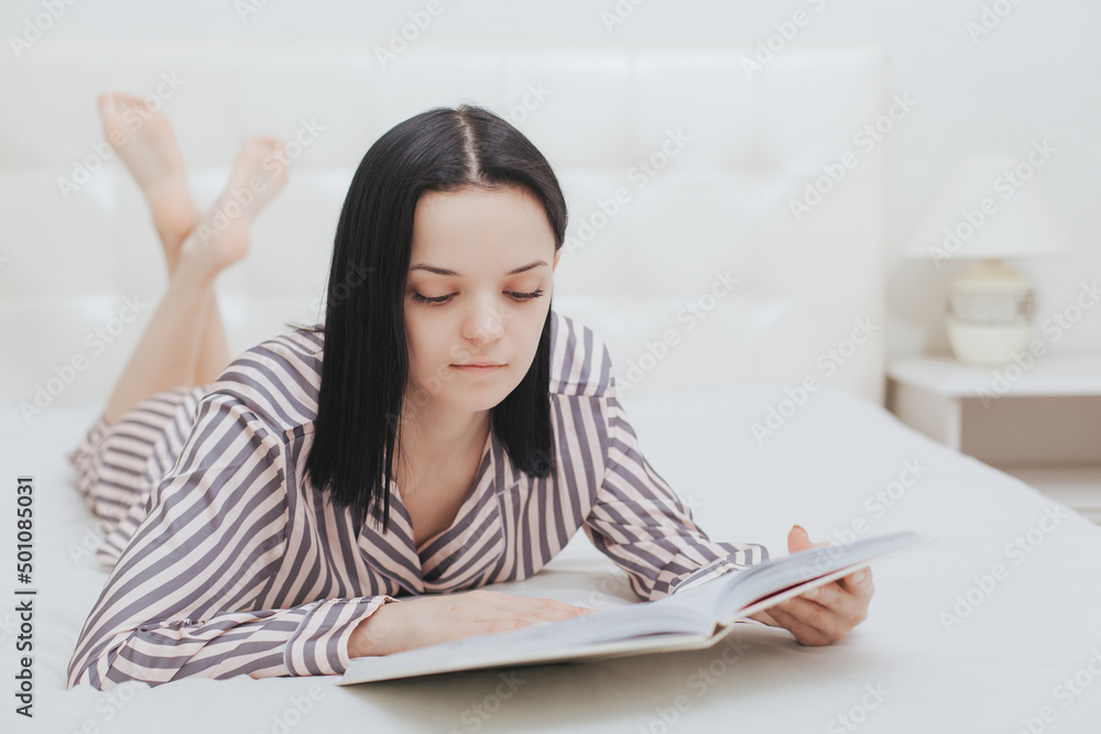 Barefoot young teenage girl lying on her bed reading a book or studying Barefoot young teenage girl lying on her bed reading a book or studying