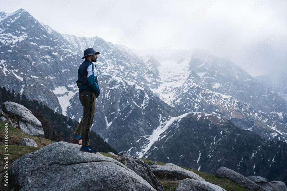 A tourist is enjoying the beautiful view of Dhauladhar Mountain ranges during a sunny day. Triund, Dharamsala, Himachal Pradesh, India.