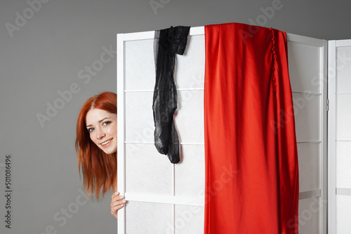 young woman peeks from behind folding screen while undressing or changing clothes photo