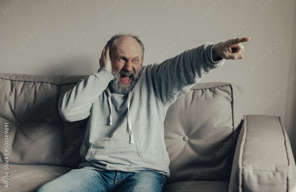 Fototapeta premium Ukrainian frightened gray-haired man saw the explosion through the window. The husband is frightened by the sounds of war outside the window. Stop the war. Pray for Ukraine.