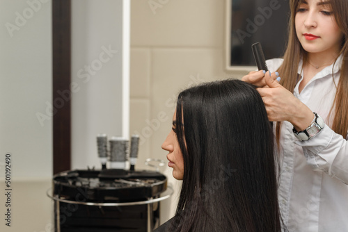 Female hairdresser making hairstyle to young brunette woman in spa salon