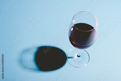 Glass of red wine on blue background with dark shadow.