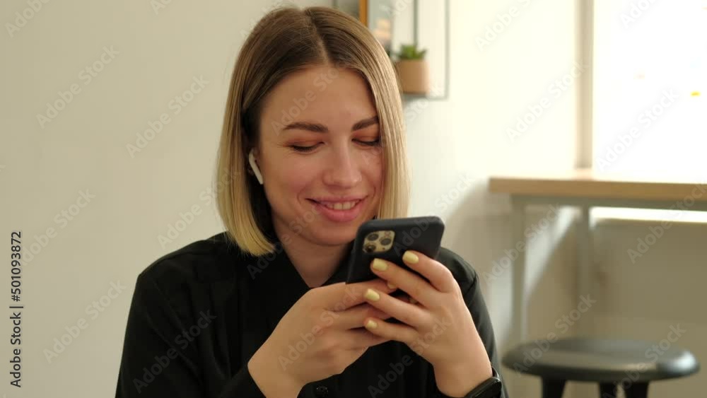 Close up video of smiling young woman sitting in cafe and typing on smartphone. Close up video of smiling young woman sitting in cafe and typing on smartphone.
