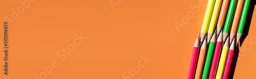 top view of colorful pencils on orange background, banner.