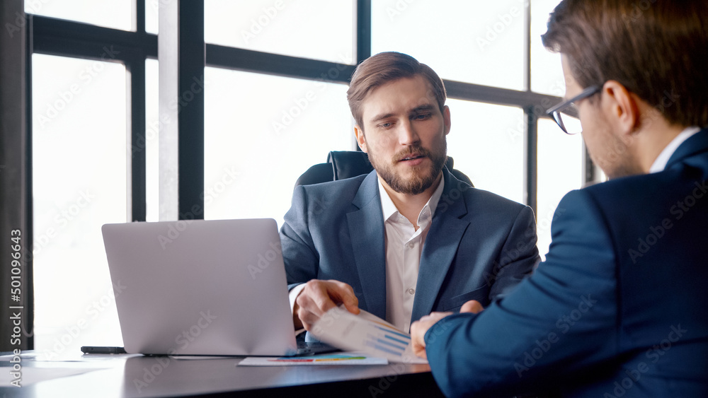 Two colleagues in suits talking at the desk Two colleagues in suits talking at the desk