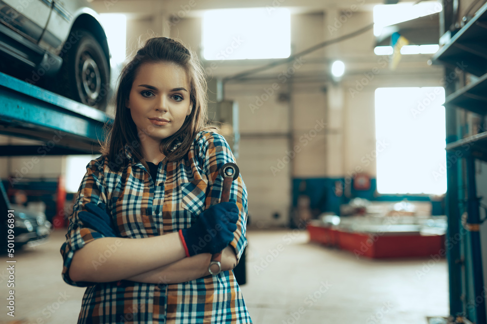Portrait of young confident girl wearing working clothes standing at auto service station, indoors. Gender equality. Emotions, work, occupation, fashion, job and hobby
