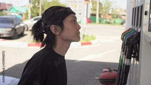Sad Asian man looks at prices at a gas station. Portrait of a customer at a gas station. The concept of rising gasoline prices