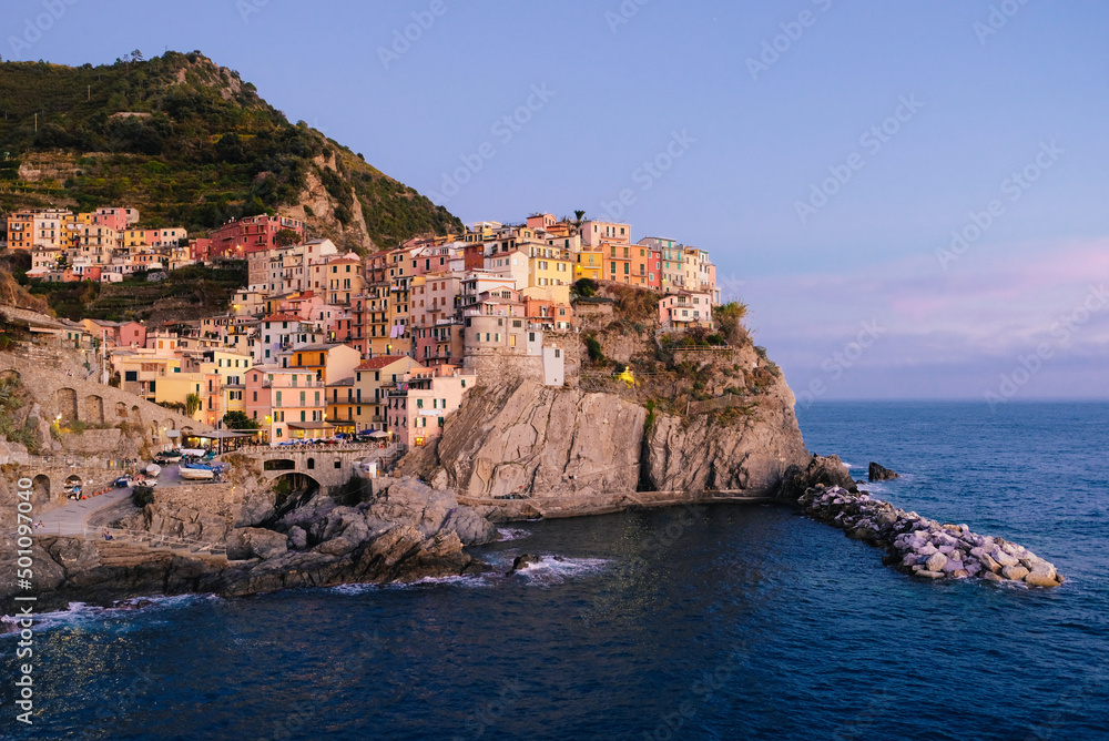 Beautiful view of rocky hills and colorful historic buildings of Manarola, tourist attraction and famous place in Liguria, Italy. Hillside over the sea at sunset.