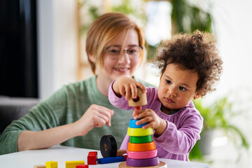 Mother looking at a child playing with an educational didactic toy. Preschool teacher with a child playing with didactic toys