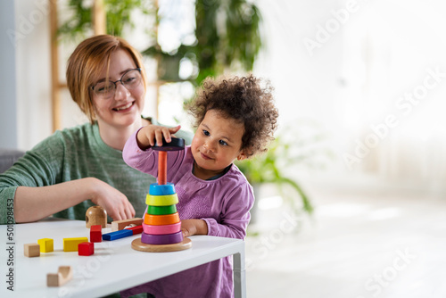 Mother looking at a child playing with an educational didactic toy. Preschool teacher with a child playing with didactic toys photo