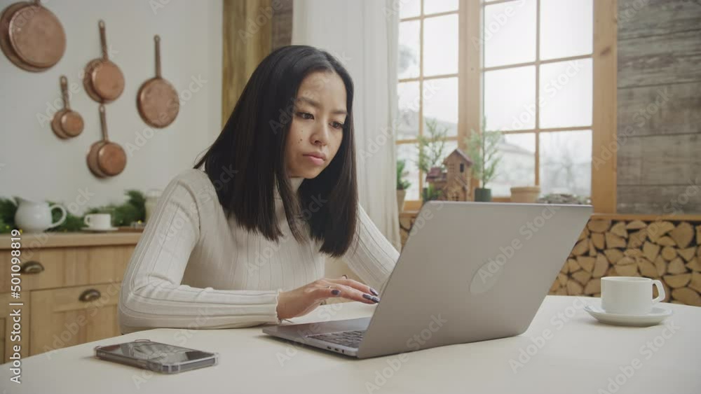 Young woman is bored using her laptop in her apartment kitchen Young woman is bored using her laptop in her apartment kitchen