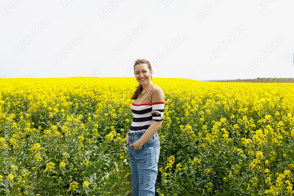 Fototapeta premium Summer portrait of a happy woman standing in a yellow field