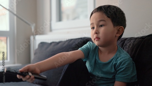 Little cute boy switch channels with remote control on TV at home