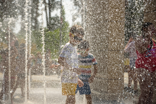 Boy having fun in water fountains. Child playing with a city fountain on hot summer day. Happy kids having fun in fountain. Summer weather. Active leisure, lifestyle and vacation