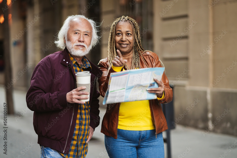 happy multiracial senior couple african woman and asian man walking through the city with a map - travel concept -