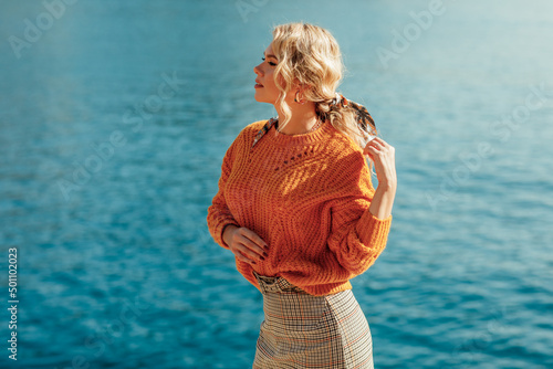 A young beautiful blonde woman walks along the embankment