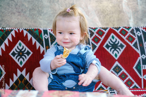 The kid has a snack on the dastarkhan. Happy child in a street cafe. Baby loves gozleme very much. Funny girl in an authentic restaurant photo