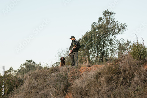 Young hunter holding his gun looking down at top of mountain