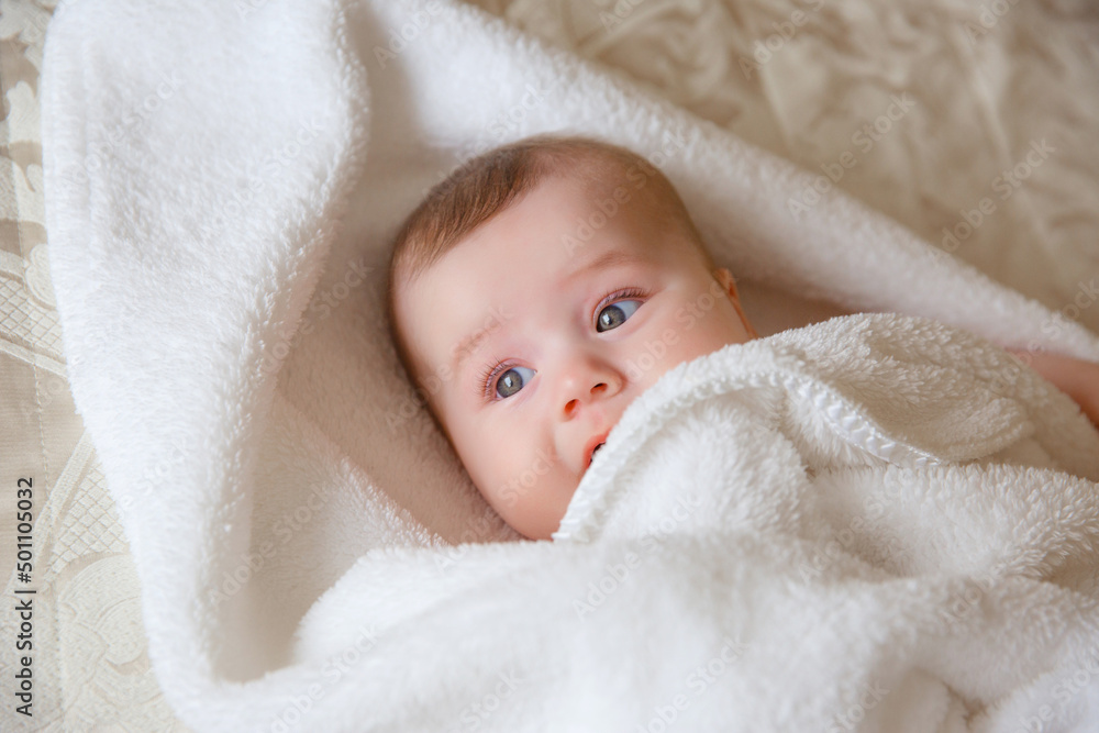 baby girl in a white towel or blanket in a white bedroom. A newborn baby is resting in bed. Portrait of a Caucasian child. The concept of children's goods baby girl in a white towel or blanket in a white bedroom. A newborn baby is resting in bed. Portrait of a Caucasian child. The concept of children's goods