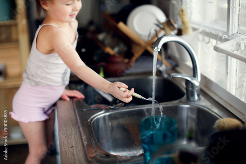 Toddler child washes his hands and fork in the sink in the kitchen, lifestyle in a real interior