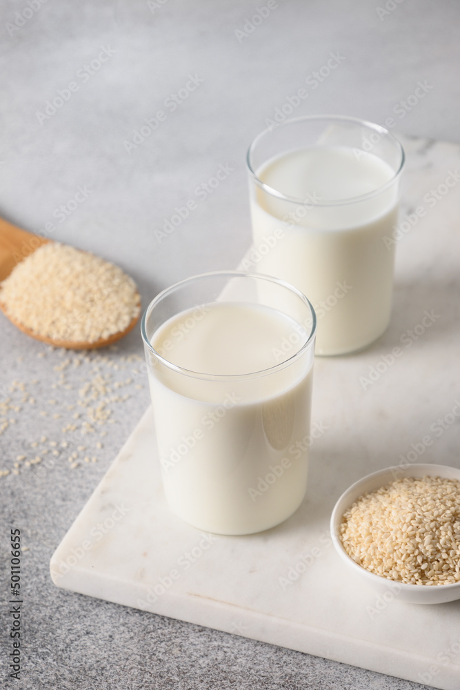 White Sesame milk in two glasses on gray background. Close up. Vegan non dairy alternative plant based milk. Vertical. White Sesame milk in two glasses on gray background. Close up. Vegan non dairy alternative plant based milk. Vertical.