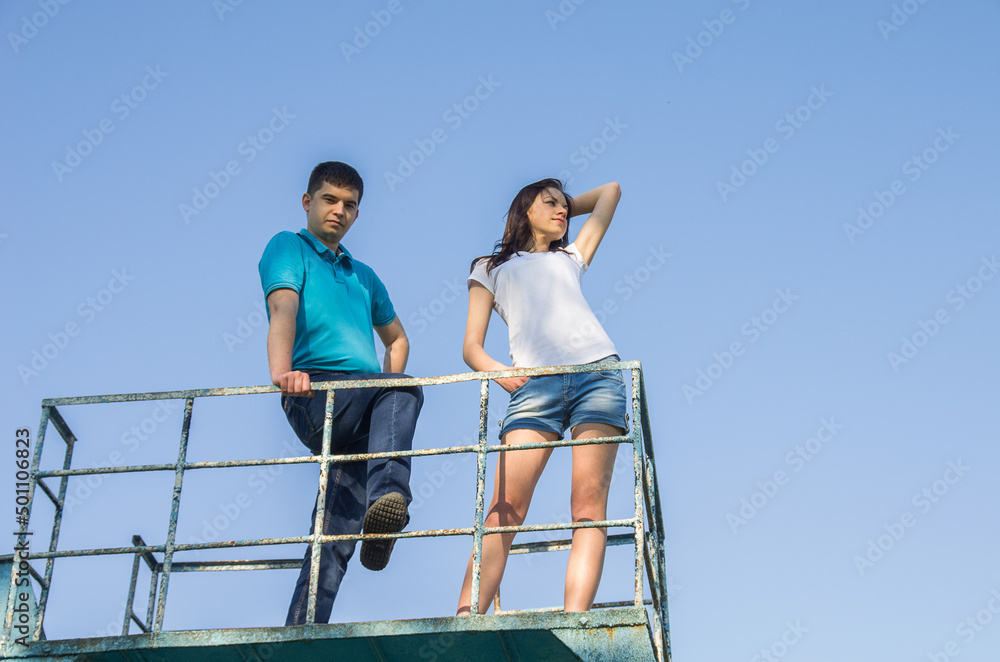 A man and a woman - a couple in love on a metal structure against a blue sky A man and a woman - a couple in love on a metal structure against a blue sky