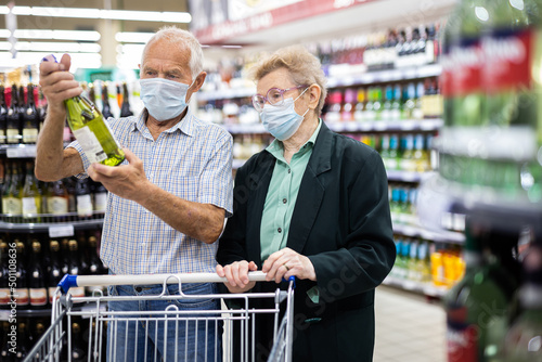 mature european spouses chooses bottle of wine in alcohol section of supermarket