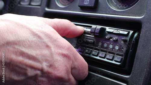The driver inserts a cassette into a cassette recorder in an old car.	