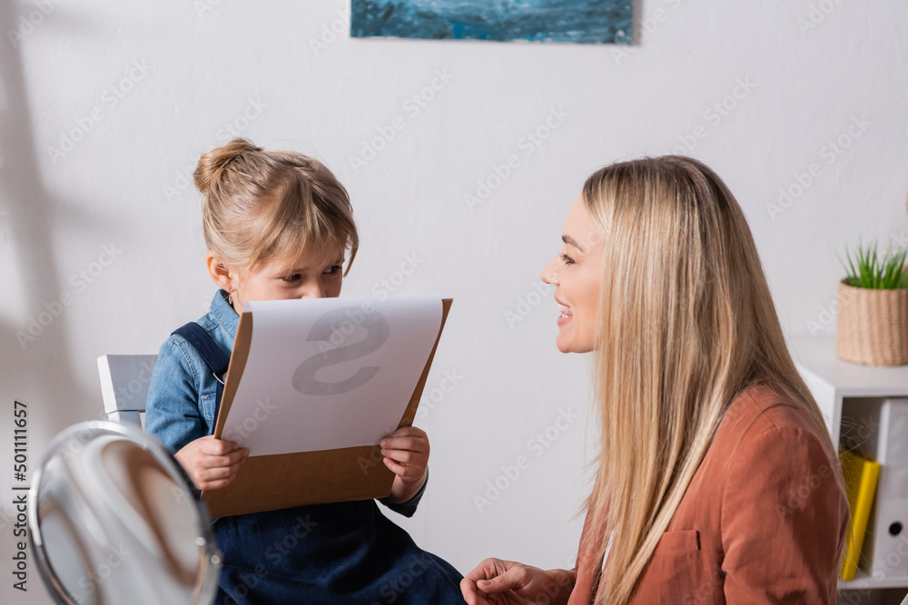 Speech therapist talking near child holding clipboard in classroom. Speech therapist talking near child holding clipboard in classroom.