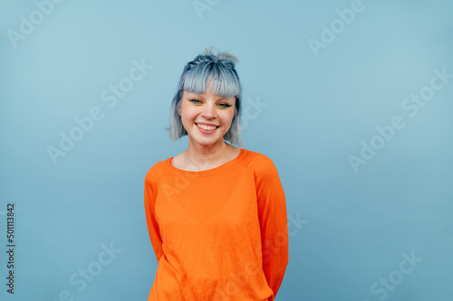 Smiling hipster girl with colored hair stands on a blue background with a happy face and looks at the camera.