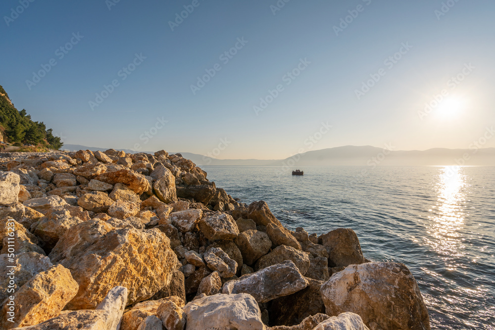 Sunset at rocky stone beach in Albania. Adriatic sea, peninsula Karaburun on horizon