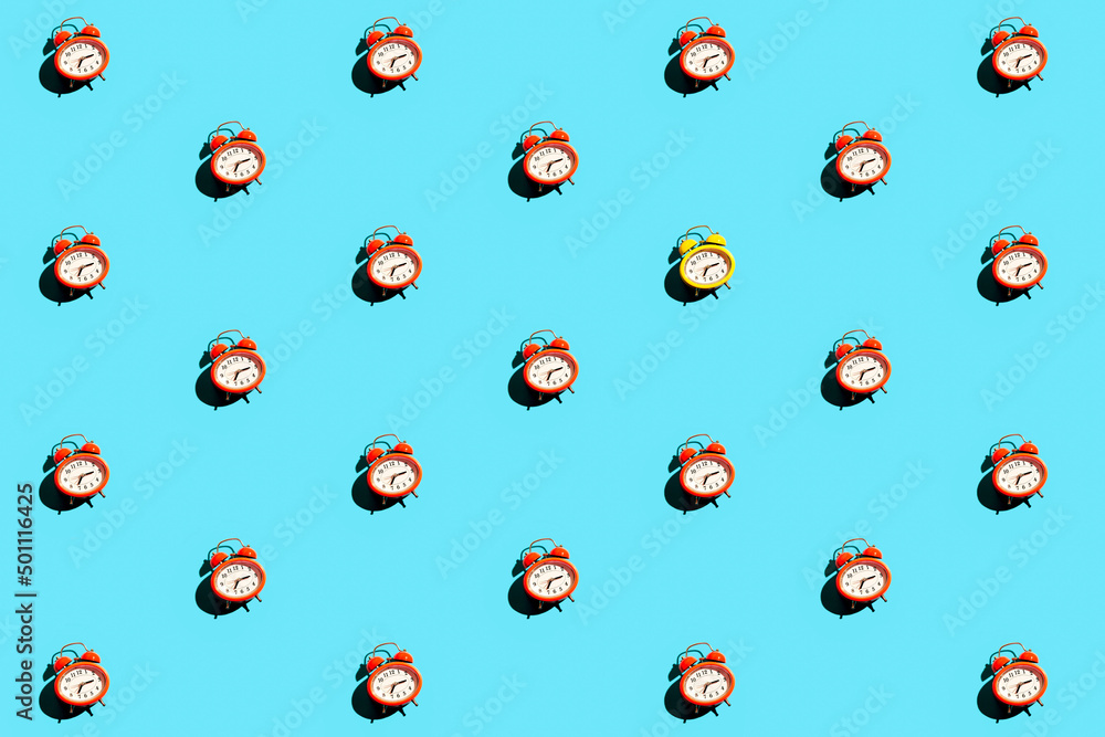 Minimalist concept flat lay with yellow and red clock. Repetitive pattern made of vintage style alarm clocks on blue background. Minimalist concept flat lay with yellow and red clock. Repetitive pattern made of vintage style alarm clocks on blue background.
