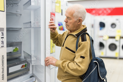 elderly grayhaired man pensioner looking refrigerator at counter in showroom of electrical appliance hypermarket department