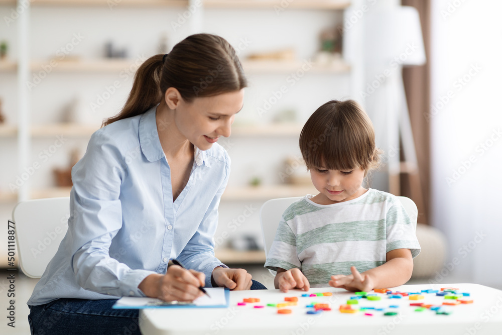 Cute little boy study to read with professional tutor, positive woman tutor helping kid and taking notes Cute little boy study to read with professional tutor, positive woman tutor helping kid and taking notes