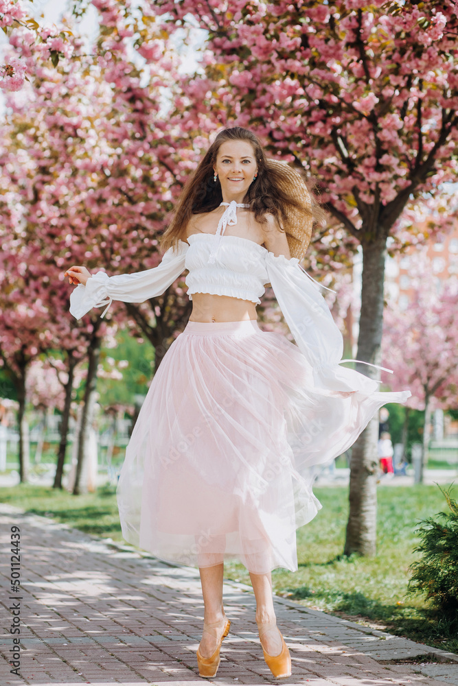 Amazing young ballerina in an pink-white dress in pointe shoes near the pink sakura tree Amazing young ballerina in an pink-white dress in pointe shoes near the pink sakura tree