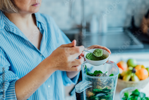 Close up woman adding wheat grass green powder during making smoothie on the kitchen. Superfood supplement. Healthy detox vegan diet. Healthy dieting eating, weight loss program. Selective focus.