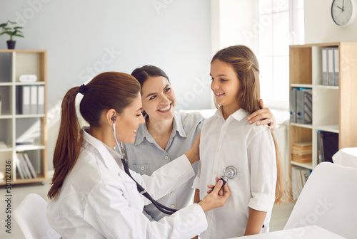 Female doctor pediatrician using stethoscope listens lungs and heart of child girl. Doctor or nurse examines teen girl who came for medical examination with her mother. Concept of pediatric medicine. photo