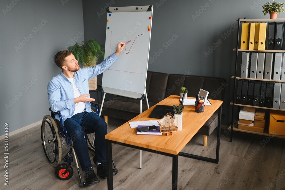 A man in a wheelchair is working in a office. The concept of work of people with disabilities. A man in a wheelchair is working in a office. The concept of work of people with disabilities.