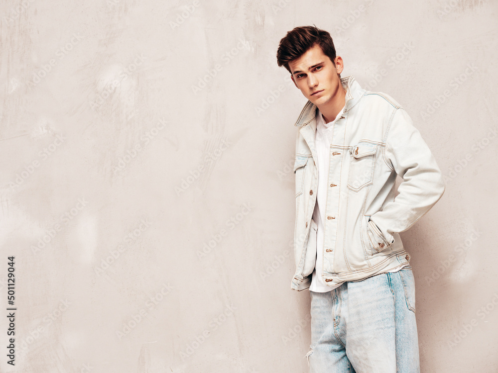 Portrait of handsome confident stylish hipster lambersexual model.Man dressed in jacket and jeans. Fashion male posing in studio near grey wall