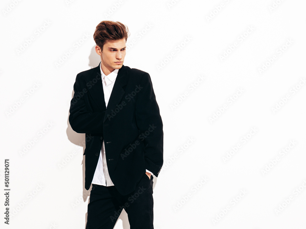 Portrait of handsome confident stylish hipster lambersexual model. Sexy modern man dressed in elegant black suit. Fashion male posing in studio near white wall. Isolated Portrait of handsome confident stylish hipster lambersexual model. Sexy modern man dressed in elegant black suit. Fashion male posing in studio near white wall. Isolated