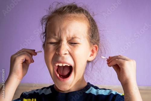 girl child in a striped turtleneck shows pain due to a cotton stick in the ear, where it is very dirty