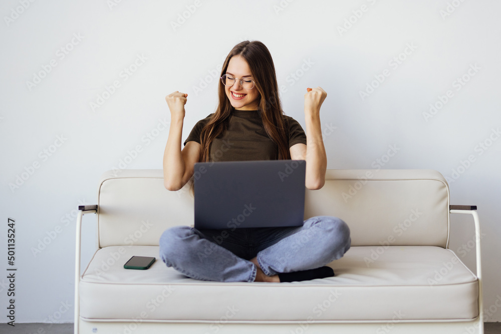 Joyful woman using laptop on the sofa with win gesture Joyful woman using laptop on the sofa with win gesture
