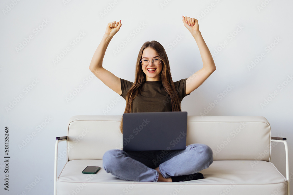 Joyful woman using laptop on the sofa with win gesture Joyful woman using laptop on the sofa with win gesture