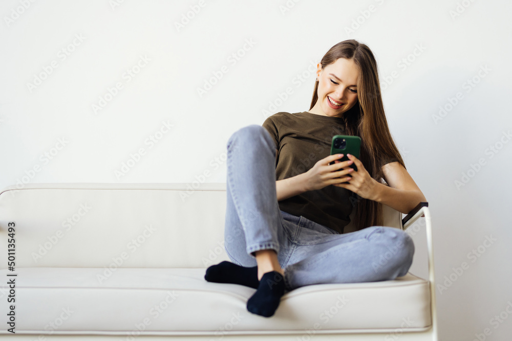 Attractive smiling woman using smart phone while sitting on the sofa at home. Communication and coziness concept. Attractive smiling woman using smart phone while sitting on the sofa at home. Communication and coziness concept.