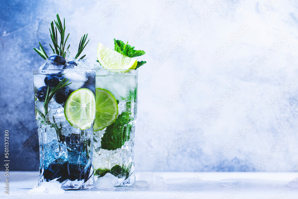 Summer cocktails or mocktails and cold drinks. Refreshing mojito drink with blueberries, blackberries, raspberries and  lime, herbs and ice on gray background - obrazy, fototapety, plakaty 