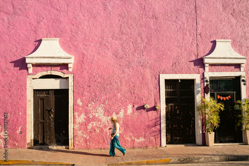Bright texture shaby pink wall. pedestrian in blue clothes walks along sidewalk. Colors of mexican street city valladolid